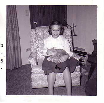 Black and white photo of a girl sitting in an easy chair with an orange tabby cat in her lap.