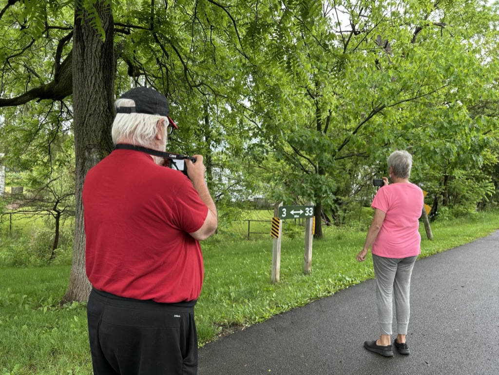 A picture of a man taking a picture of a woman taking a picture of a trail sign
