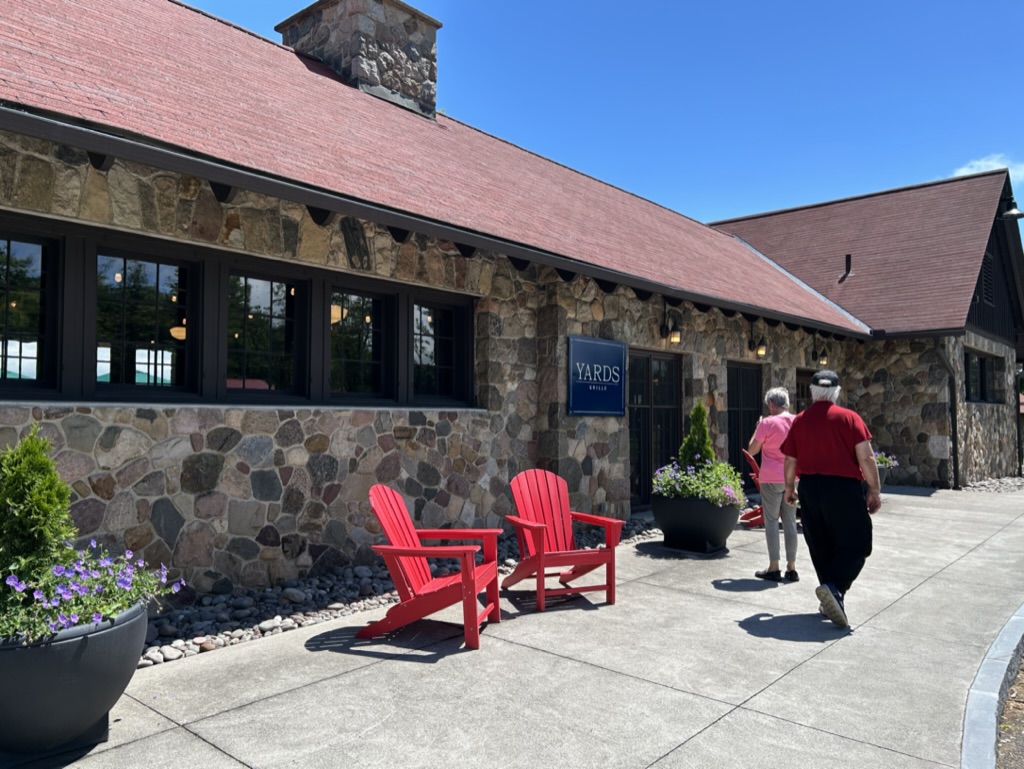 A long, low brick building with shingled roof and red adirondack chairs out front
