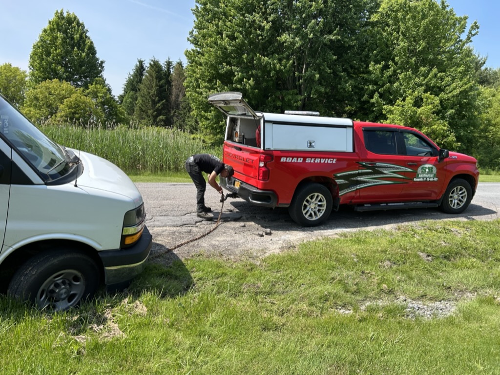 A red tow van on the side of the road, preparing to pull a white van out of the ditch