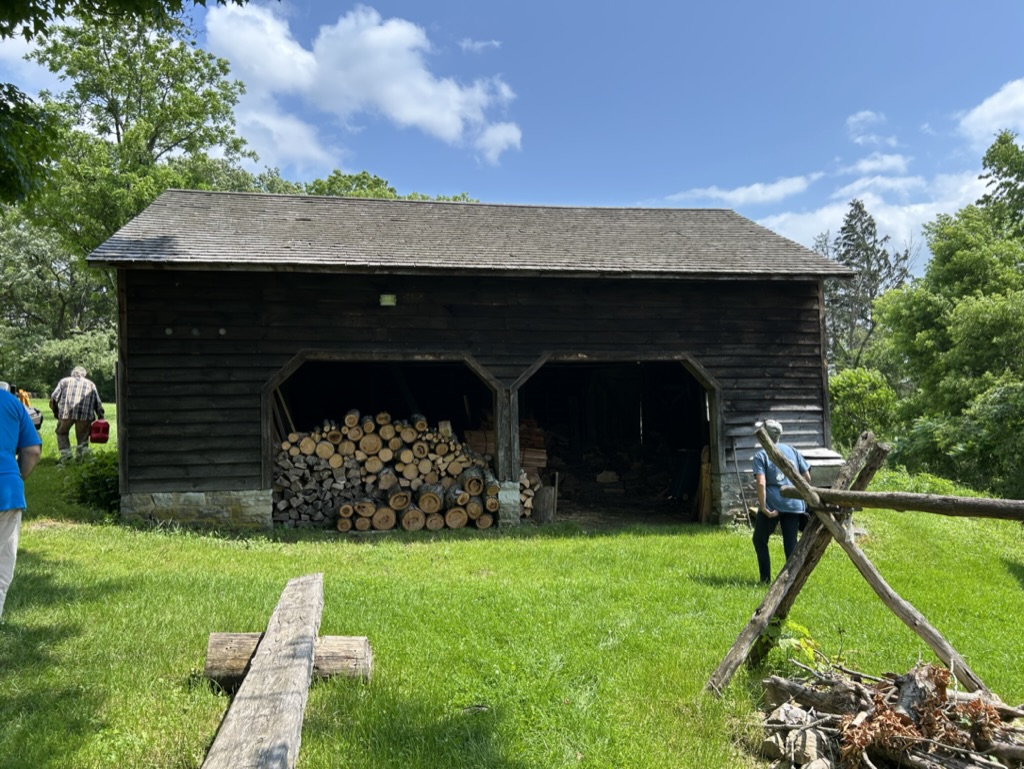 A large wooden garage-type building with two open doorways. One side is filled with firewood.