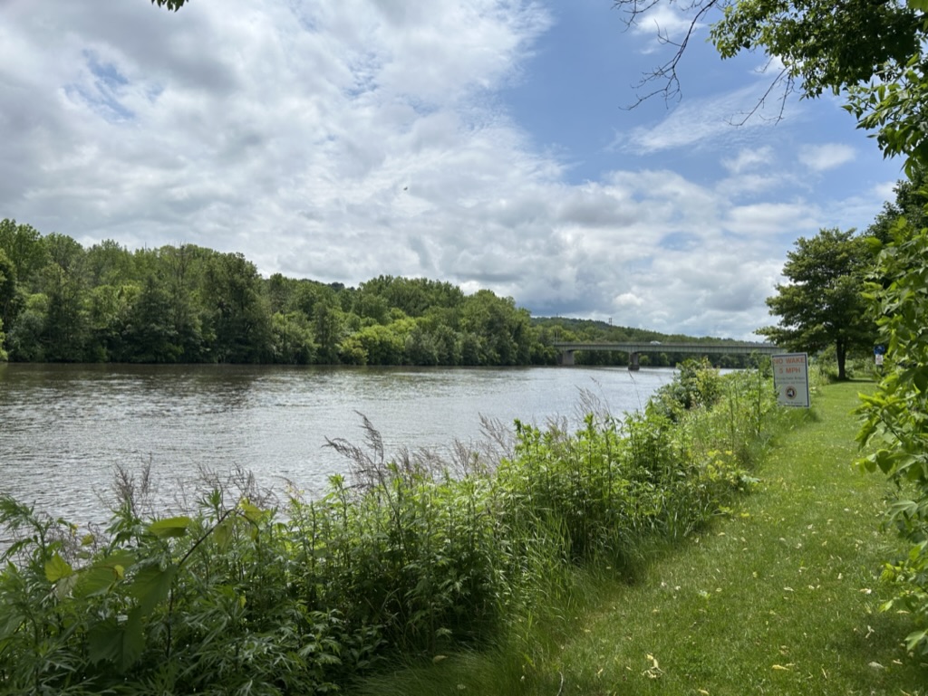 Vew of a peaceful canal with grass and trees on either side. In the distance a bridge crosses the canal