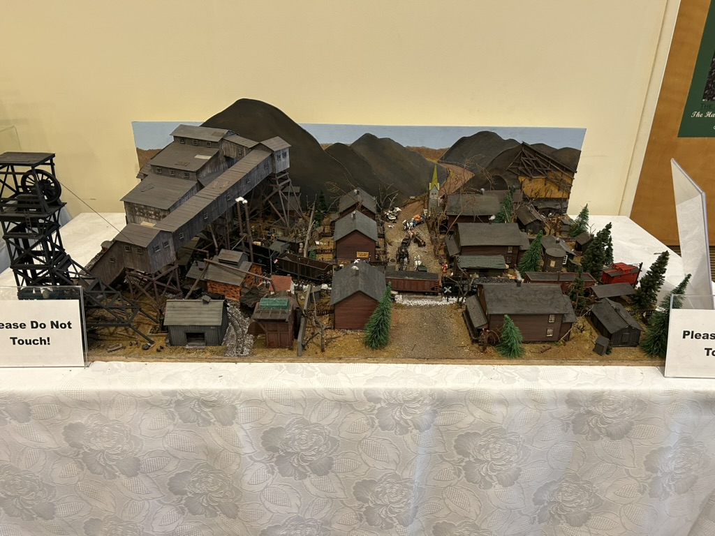 Model of a coal mining town, showing the coal shute and mine entrance on the left, and various support buildings beside it and mountains behind.